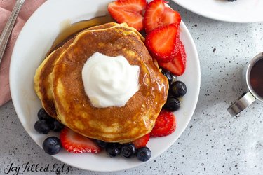 Keto Buttermilk Pancakes with fruit and whipped cream on white plate