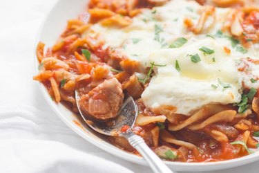 Slow Cooker Lasagna Soup in a white bowl with spoon topped with melted mozzarella cheese.