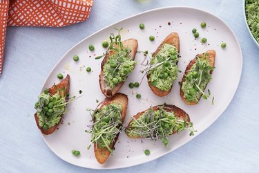 an overhead photo of a white plate with 6 pieces of toast with avocado and sprouts