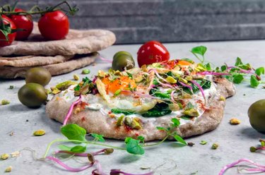 Egg Veggie Pita Pizza on a counter top with tomatoes and fresh herbs
