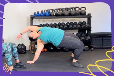 a trainer wearing a teal tank top and gray leggings does a crab bridge with reach during a full-body strengthening workout in a gym in front of a rack of kettlebells and dumbbells