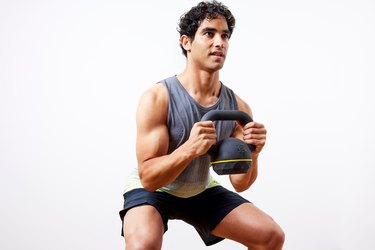 young fit athlete with short hair and defined biceps muscles does a KB squat as part of a kettlebell leg workout