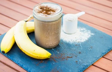 Protein blended coffee with white measuring cup and bananas on a blue mat