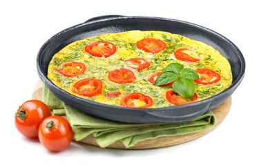 Quick tomato and basil frittata in a pan with tomatoes against white background