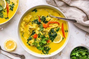 A white bowl of yellow Detox Soup with veggies and lemon