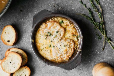 An overhead photo of a cast iron bowl of French Onion Soup surrounded by slices of baguette