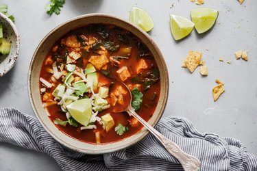 a bowl of Mexican Tortilla Soup with avocados and limes next to a cloth napkin