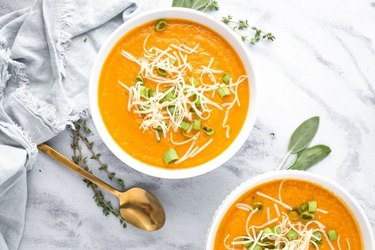 Two bowls of Carrot Parsnip Soup on a white marble counter next to a gold spoon