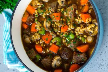 An overhead photo of a blue bowl of Beef Barley Soup with carrots and mushrooms