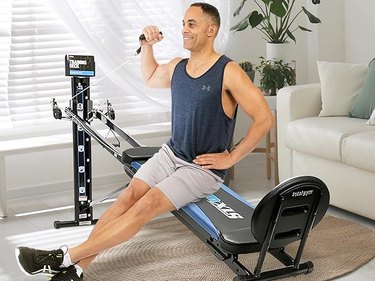 an adult wearing gray shorts and a navy tank top performs one of the best exercises on the total gym in a living room