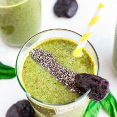 Overhead view of a glass of a green prune smoothie with a yellow striped straw
