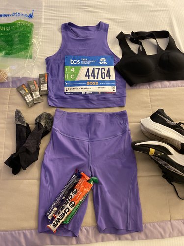 A photo of a purple tank top and shorts laying flat with sneakers socks a sports bra and running gels around it.