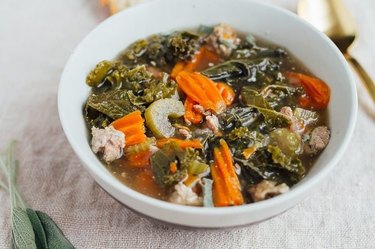 an overhead photo of a white bowl of Sausage Kale Soup next to a gold spoon and slices of bread