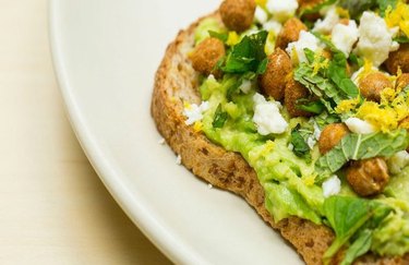 a close up photo of a blue zone-inspired breakfast recipe of crunchy spiced chickpea toast on a white plate with feta crumbles