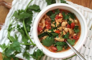 blue zone breakfast recipe savory Tuscan oatmeal in a white bowl with a spoon, parsley leaves, tomatoes and white beans