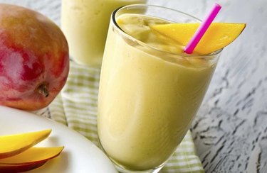 Blue zone breakfast recipe sunshine smoothie in a glass with a pink straw and mango slices