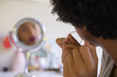 behind the shoulder view of a person with black coily hair putting in a hoop earring and wondering about their smelly ear piercing