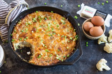 High Protein Cauliflower Breakfast Skillet Casserole in a black skillet with a bowl of brown eggs and cauliflower florets