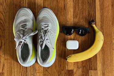 Lululemon's Blissfeel 2 shoe alongside airpods, Goodr sunglasses and a banana on hardwood background.
