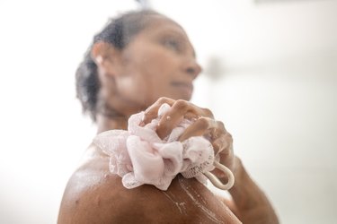 a close up of an adult using a light pink washcloth in the shower