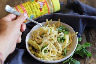 bowl of spaghetti with peas with Bragg nutritional yeast on the side