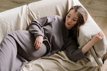 pregnant person lying on a white couch in need of a natural remedy for nausea