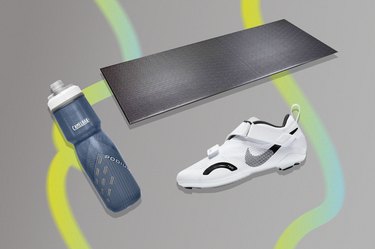collage of an exercise mat, water bottle and cycling shoes on a gray background to demonstrate the best exercise bike accessories.