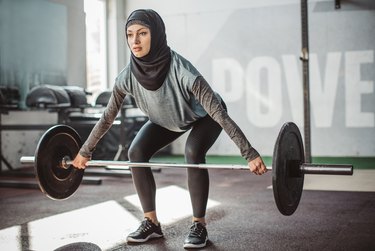 Woman wearing hijab lifting a barbell at the gym to demonstrate if increasing weight in each set can maximize muscle.