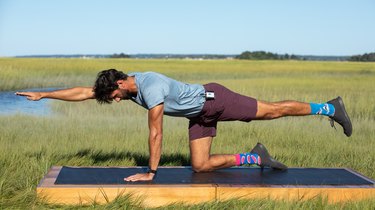 Man exercising a bird dog on a yoga mat platform near lakes and fields