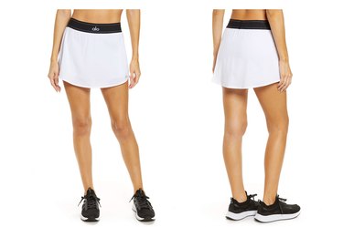 White Alo brand tennis skirt — shown on a model from the waist down, who is also wearing black shoes