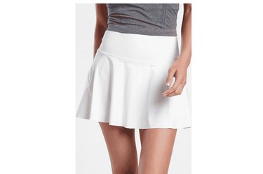 Model, shown from the waist down, wearing a white Athleta brand tennis skirt and a grey top