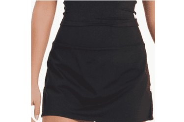 Model, shown from the waist down, wearing a black Vuori brand tennis skirt and a black top