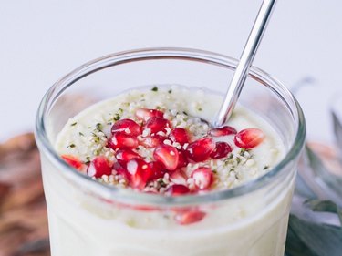 Avocado Pineapple Smoothie with hemp seeds and pomegranate on top in glass cup with steel straw