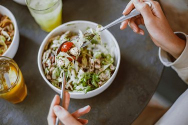an overhead photo of a person eating a salad in a white bowl as a strategy for belly fat loss