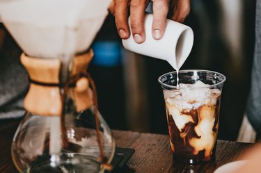 hand pouring oat milk into cup of iced coffee