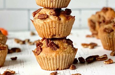 A closeup of two morning glory muffins on a white table with pecans scattered around it.