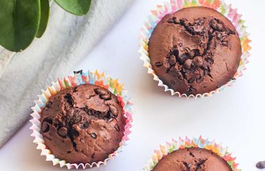 Fresh chocolate muffins in colorful muffin liners placed on a white table.