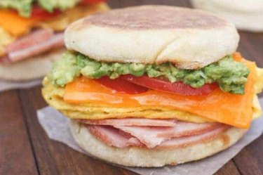 egg, ham and avocado breakfast sandwich recipe on parchment paper on wooden table