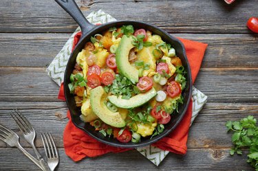 egg and avocado skillet breakfast recipe topped with sliced baby tomatoes, avocados and fresh herbs.
