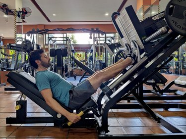 side view of person at the gym using the leg press with their feet hanging off, doing a calf raise, to target to calf muscles
