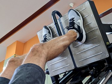 close up of a person's legs with their feet higher up on the leg press to target their glutes and hamstrings