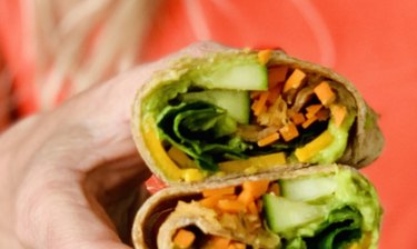 California Kraut and Cheddar Wrap with greens and cucumbers in front of an orange background