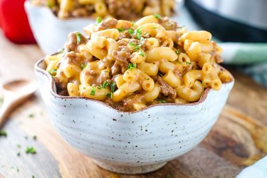 Scalloped edge white speckle bowl filled with elbow pasta and ground meat.