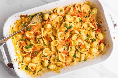 White casserole dish filled with shell pasta and baby tomatoes in feta cheese sauce