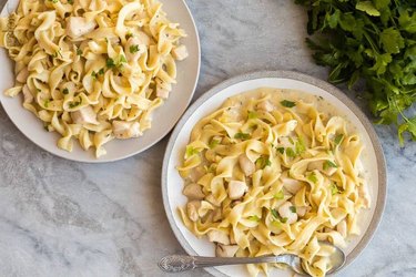 Egg noodles with diced chicken on white plate on gray marble background
