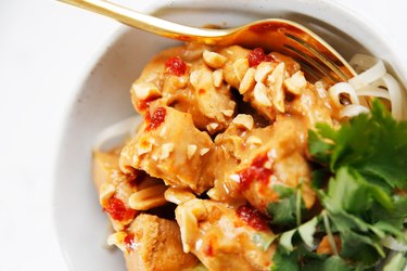 Chicken pieces covered in Thai peanut sauce in a white bowl.