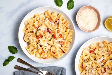 Bowtie pasta with tomato and diced chicken on a white plate.