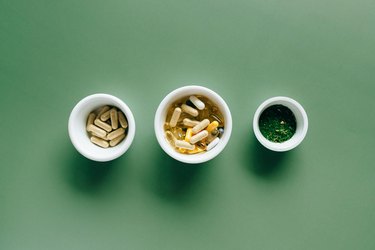 an overhead photo of three white ceramic bowls of herbal supplements on a green background