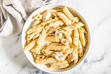 Penne pasta and diced chicken in a cheesy sauce topped with black pepper in a white bowl