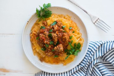 Spaghetti squash topped with meat bolognese sauce and parsley on a white plate.